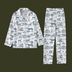 K&ouml;nnte beinhalten: Wei&szlig;es Pyjama-Set mit blauem Pferde- und Hufeisenmuster. Das Set besteht aus einem Hemd mit Kn&ouml;pfen und einer passenden Hose. Das Design zeigt Pferde, Reiter und l&auml;ndliche Szenen. Der Pyjama ist aus einem weichen, leichten Stoff gefertigt.