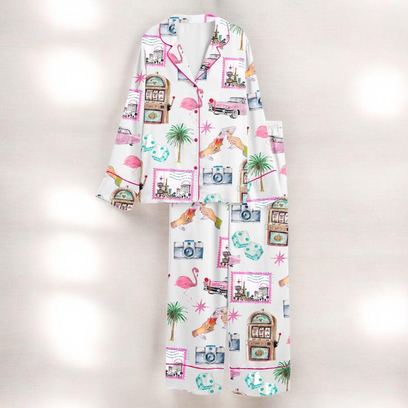 Puede incluir: Conjunto de pijama blanco con un estampado repetido de flamencos rosas, coches antiguos, m&aacute;quinas tragamonedas, c&aacute;maras, dados y palmeras. El conjunto incluye una camisa con botones con ribete rosa y pantalones a juego.