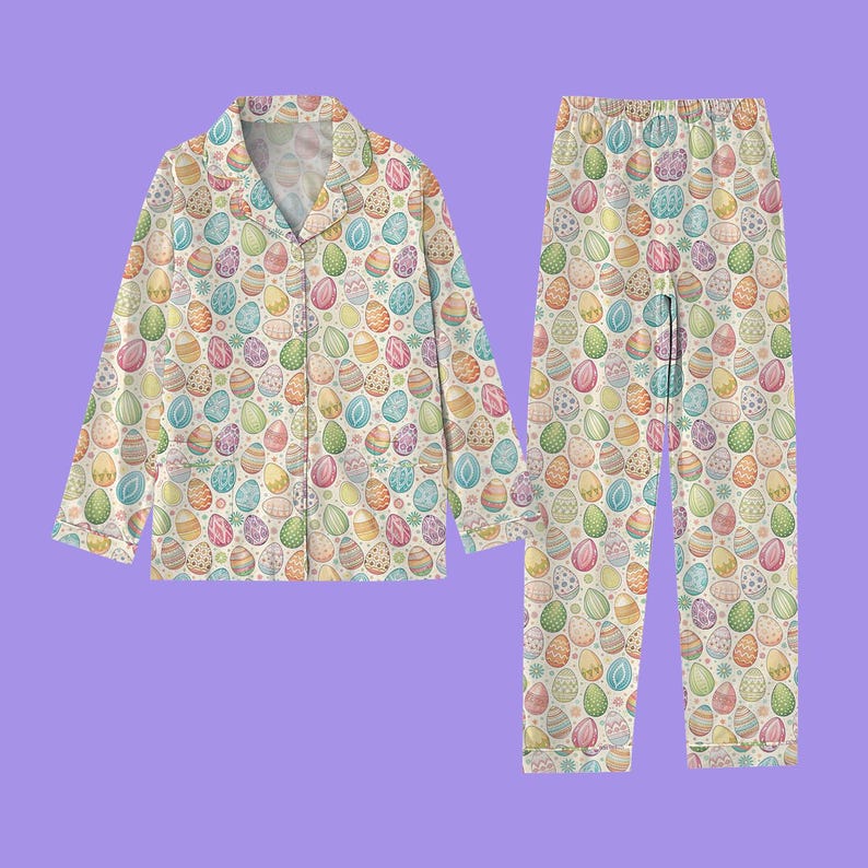 May include: A two-piece pajama set featuring a repeating pattern of colorful Easter eggs on a cream background. The long-sleeved top has a button-down front and a notched collar. The matching pants have an elastic waistband.