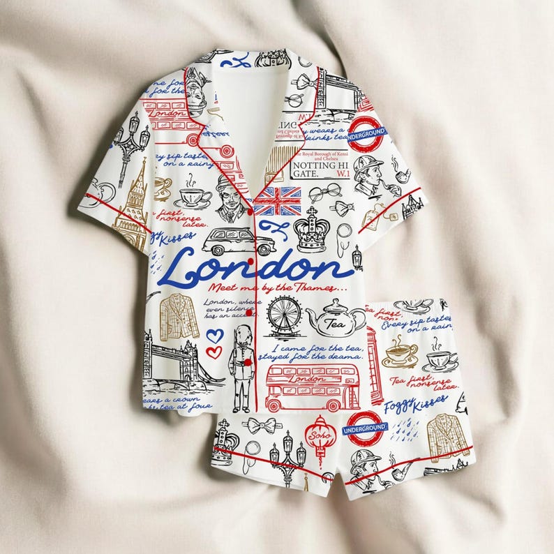 May include: A white London-themed pajama set featuring a short-sleeved shirt and shorts, both with red piping. The print includes illustrations of London landmarks such as the London Eye, a red double-decker bus, and the Union Jack flag.