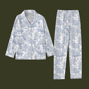 May include: A white and blue toile-patterned pyjama set depicting a safari scene. The set comprises a long-sleeved, button-down shirt and matching trousers. The shirt has a notched collar and the trousers have an elasticated waistband.