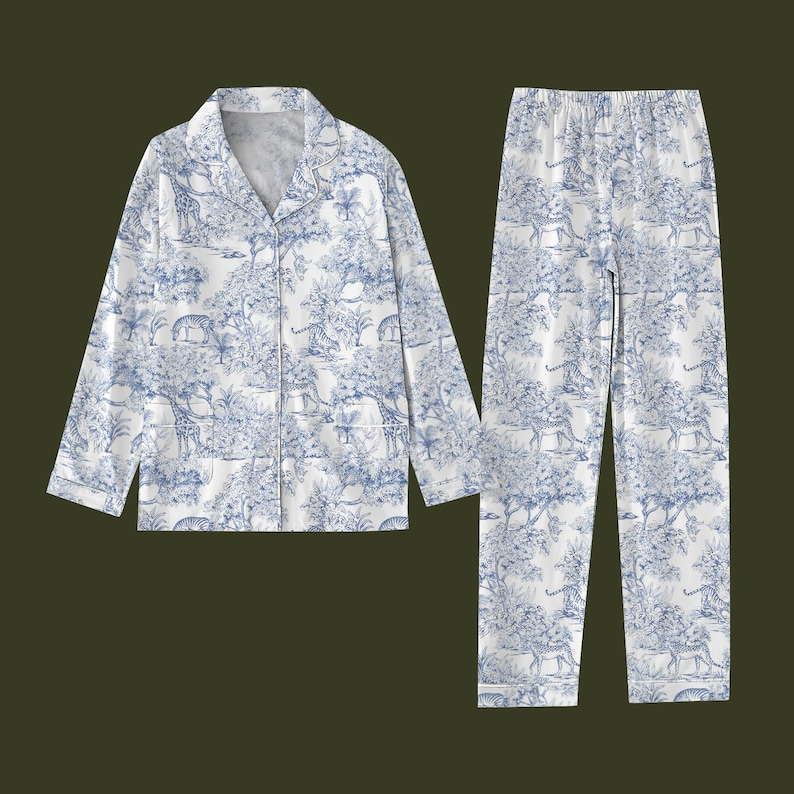 May include: A white and blue toile-patterned pyjama set depicting a safari scene. The set comprises a long-sleeved, button-down shirt and matching trousers. The shirt has a notched collar and the trousers have an elasticated waistband.