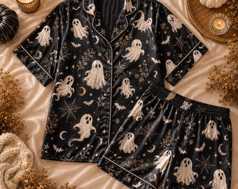 Op de afbeelding: Een zwarte pyjamaset bestaande uit een shirt met korte mouwen en knoopsluiting en een bijpassende short. De stof is bedrukt met een patroon van witte spoken, spinnenwebben, maansikkels, vleermuizen en kleine bloemtakjes.