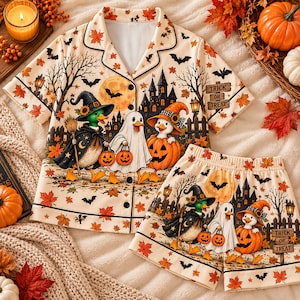May include: A cream-colored short-sleeve button-down pajama shirt and matching shorts set featuring a Halloween print of ducks dressed as a witch, a ghost, and a pumpkin, with bats, autumn leaves, a haunted house, and a sign reading TRICK OR TREAT.