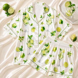 May include: A white short-sleeve button-down pajama shirt and matching elastic-waist shorts set featuring a repeating print of green lime slices, mint leaves, and stemmed cocktail glasses filled with ice and citrus garnishes with green piping.