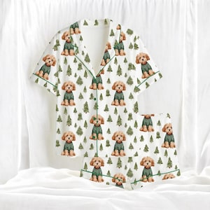 May include: White pajama set with a repeating pattern of brown dogs wearing green sweaters and green Christmas trees. The short-sleeved top and shorts have green trim.