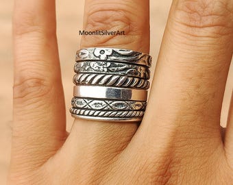Könnte beinhalten: Ein Stapel aus sechs Silberringen mit verschiedenen Texturen und Mustern, darunter florale Motive, gedrehte Seildesigns und ein glattes, poliertes Band. Der Text MoonlitSilverArt ist über den Ringen sichtbar. Jeder Ring hat ein oxidiertes Finish.