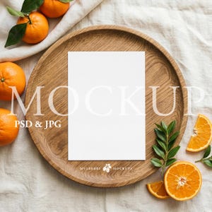 Puede incluir: Una bandeja de madera con una tarjeta blanca en blanco, naranjas frescas y hojas verdes. El texto "MOCKUP PSD & JPG" es visible. El logotipo de Mulberry Mockups está en la parte inferior.