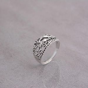 Può includere: Un anello d'argento con un design a filigrana ornato. L'anello presenta un motivo dettagliato di linee e forme a vortice, creando un effetto traforato. La fascia dell'anello è liscia e lucida e lo stile generale è vintage.