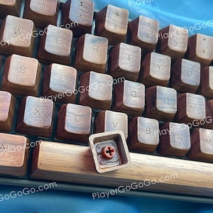 May include: A close-up shot of a wooden mechanical keyboard. The keycaps are a rich brown, each with white lettering. One keycap is detached, showing the internal components. A separate "Home" keycap is also visible.