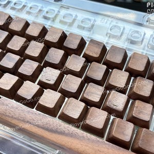 May include: Close-up of a mechanical keyboard with wooden keycaps. The keycaps are a warm brown color, and the keyboard has a clear plastic frame. The text "PlayerGoGoGo.com" is visible on the keyboard.