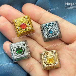 Può includere: Quattro anelli quadrati con disegni ornati e pietre preziose. Un anello d'oro presenta un leone e una gemma rossa, un altro ha un'aquila e una gemma blu, un terzo ha un serpente e una gemma verde, e l'ultimo ha una gemma gialla e un motivo solare.