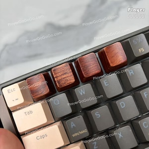 Puede incluir: Primer plano de un teclado mecánico con teclas de madera personalizadas. Las teclas son de color marrón oscuro con un patrón de vetas de madera visible. El teclado tiene un marco gris oscuro y teclas grises claras y negras. El texto "PlayerGoGoGo.com" es visible.