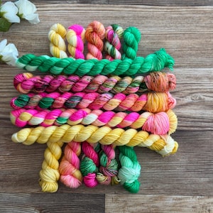 May include: A collection of hand-dyed yarn mini skeins arranged in horizontal rows. The yarn features a vibrant palette of neon pink, bright yellow, emerald green, and variegated multi-colored strands, showcasing a twisted texture throughout.