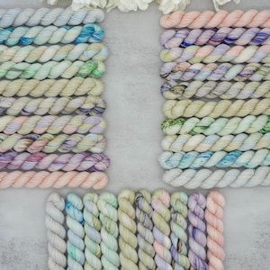 May include: A collection of small, twisted skeins of yarn arranged in three groups. The yarn features a palette of soft pastel colours including light blue, mint green, pale pink, lavender, and cream, with some skeins showing variegated speckles.