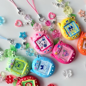 May include: A collection of colorful digital pet keychains featuring various character screens, each attached to a beaded lanyard with translucent flower, heart, and star-shaped charms. The devices are yellow, pink, blue, green, and red.