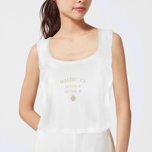 May include: White crop top with a square neckline. The top features the text "MALIBU, CA" along with coordinates and a seashell graphic in a light brown color.
