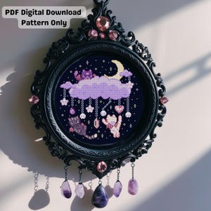 Op de afbeelding: Een ingelijste kruissteek met katten, wolken en sterren tegen een donkerblauwe achtergrond, met een halve maan en hangende bedels. Het zwarte frame heeft roze accenten en hangende amethiststenen. Tekst: PDF Digital Download Pattern Only.