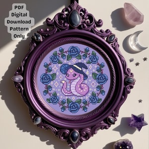 May include: A framed cross-stitch pattern featuring a purple snake wearing a witch hat, surrounded by blue roses. The frame is a dark purple with decorative accents. Text in the upper left corner reads "PDF Digital Download Pattern Only."