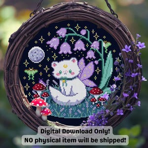 Op de afbeelding: Een kruissteekontwerp van een witte kat met vleugels, zittend in een veld met paddenstoelen en bloemen, onder een maanverlichte hemel. Het ontwerp is omlijst in een geweven krans. Tekst: "ALLEEN DIGITALE DOWNLOAD! Er wordt geen fysiek item verzonden!"
