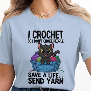 May include: Light blue t-shirt with the text "I Crochet so I don't choke people. Save a life... Send Yarn." A cartoon black cat sits in a blue basket filled with colorful yarn balls.