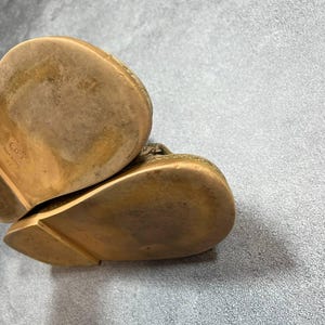 May include: Close-up of the soles of two gold-colored leather shoes. The soles show wear and tear, with a textured surface and a slight curve. The shoes appear to be a slip-on style.