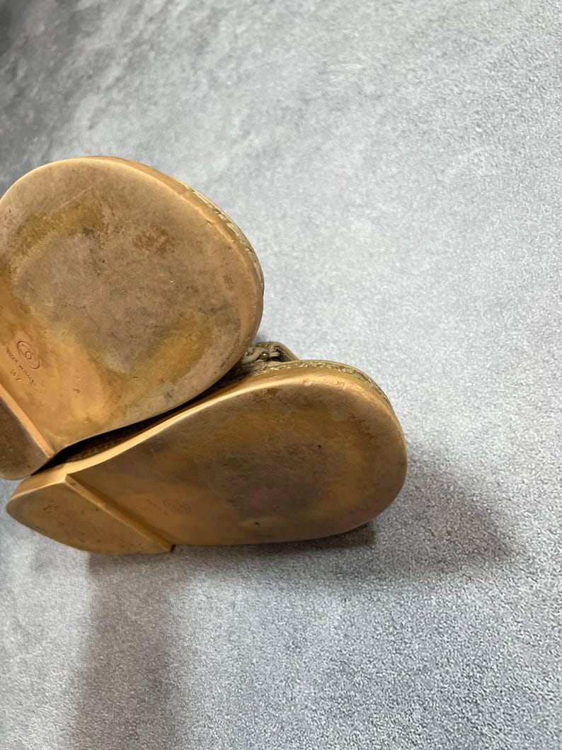 May include: Close-up of the soles of two gold-colored leather shoes. The soles show wear and tear, with a textured surface and a slight curve. The shoes appear to be a slip-on style.