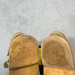 May include: A pair of beige sandals with a textured strap and a buckle closure. The soles are worn and show the size 37, and the brand logo. The sandals are made in Italy.