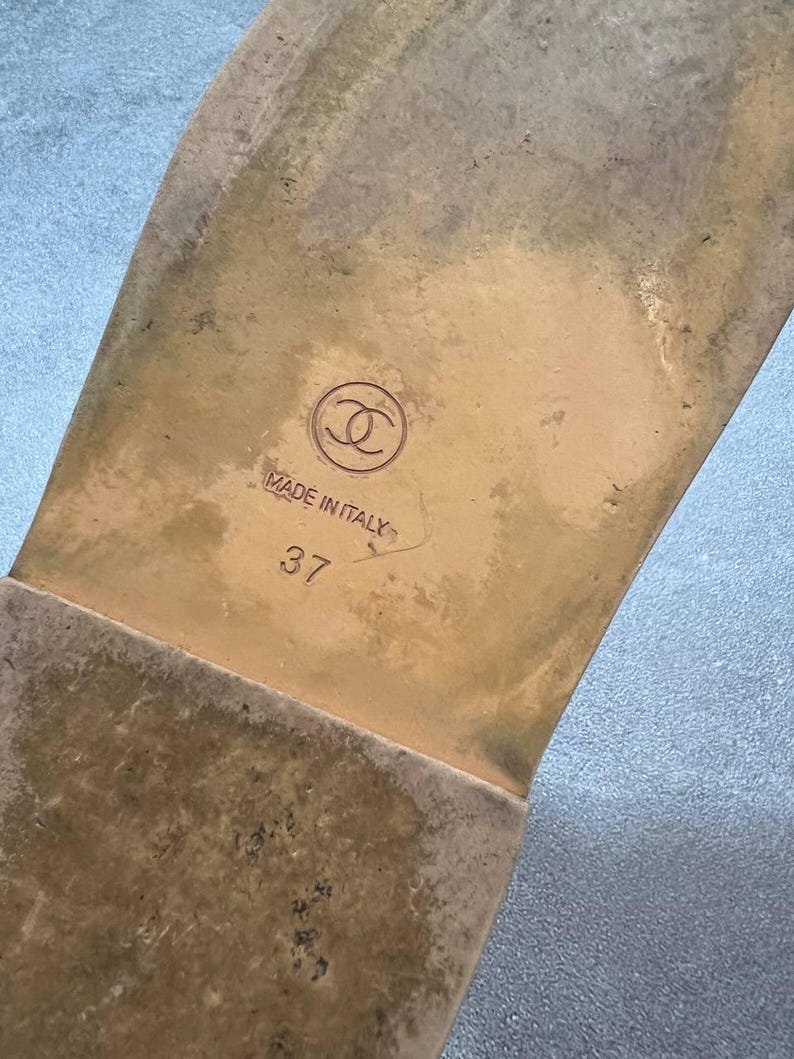 May include: Close-up of the sole of a sandal. The sole is a light brown color with a worn appearance. The brand logo is visible, along with the text "MADE IN ITALY" and the size "37".