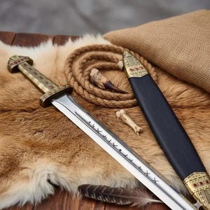 May include: A detailed image of a Viking sword with a silver blade and ornate gold-colored hilt. The sword rests on a fur-like surface, next to a black sheath with gold accents. A feather and bone fragments are also present.