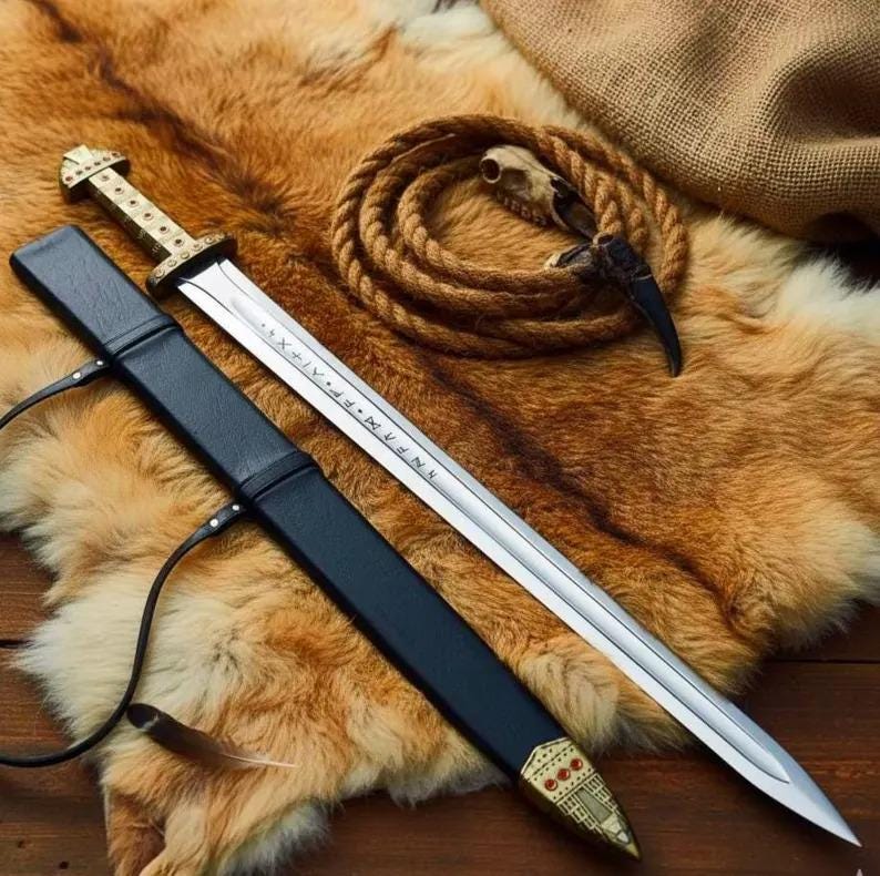 May include: A Viking-style sword with a silver blade and a gold-colored hilt, resting in a black leather sheath. The blade has etched inscriptions. The sword is displayed on a brown fur rug, with a coiled rope and a small skull in the background.