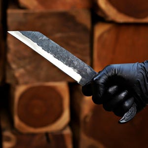 May include: A fixed-blade knife with a dark, textured, hammered metal finish on the upper portion of the blade and a polished, sharp cutting edge. The handle features a curved, ergonomic design with a metallic, patterned grip texture.