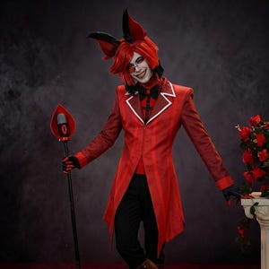 Może przedstawiać: Kostium cosplay składający się z czerwonego fraka w paski z białymi klapami, czarnej muszki i czerwonej koszuli. Strój zawiera czarne spodnie, brązowe buty z czerwonymi akcentami oraz czarną laskę zwieńczoną czerwonym elementem mikrofonu.