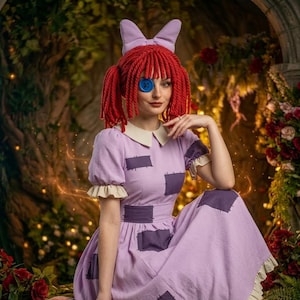 Pode incluir: Um vestido roxo claro com remendos roxo escuro, gola branca e mangas com babados. O traje inclui uma peruca de lã vermelha com marias-chiquinhas, uma faixa de cabeça com laço roxo claro e um botão azul sobre um olho como acessório.
