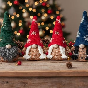 May include: Four handmade Christmas gnomes with crochet bodies and pointed hats. The hats are green, red, and blue, adorned with white snowflake and star patterns. The gnomes have long white or black braids and gray beards, set on a wooden surface.