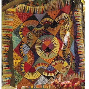 May include: A colorful patchwork quilt with a geometric design featuring sunbursts and circles. The quilt is made of various fabrics in shades of red, yellow, blue, green, and brown. The quilt is hanging on a tree branch and is surrounded by greenery.