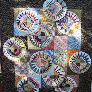 May include: A handmade quilt featuring a geometric design with circular and square patchwork. The quilt showcases a variety of fabrics in shades of blue, red, yellow, and green, with a dark brown border. The circular patterns resemble sunbursts.