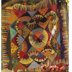 May include: A colourful patchwork quilt featuring a range of geometric patterns and designs. The quilt is made from different fabrics in shades of red, yellow, blue, green, and brown. The quilt is hanging on a wall outside, with a teapot and flowers in the foreground.