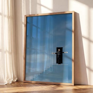 May include: A rectangular framed wall art piece featuring a surreal blue sky background with a set of white stairs leading to a dark doorway. A figure dressed in black stands in the doorway with arms outstretched against the bright blue sky.
