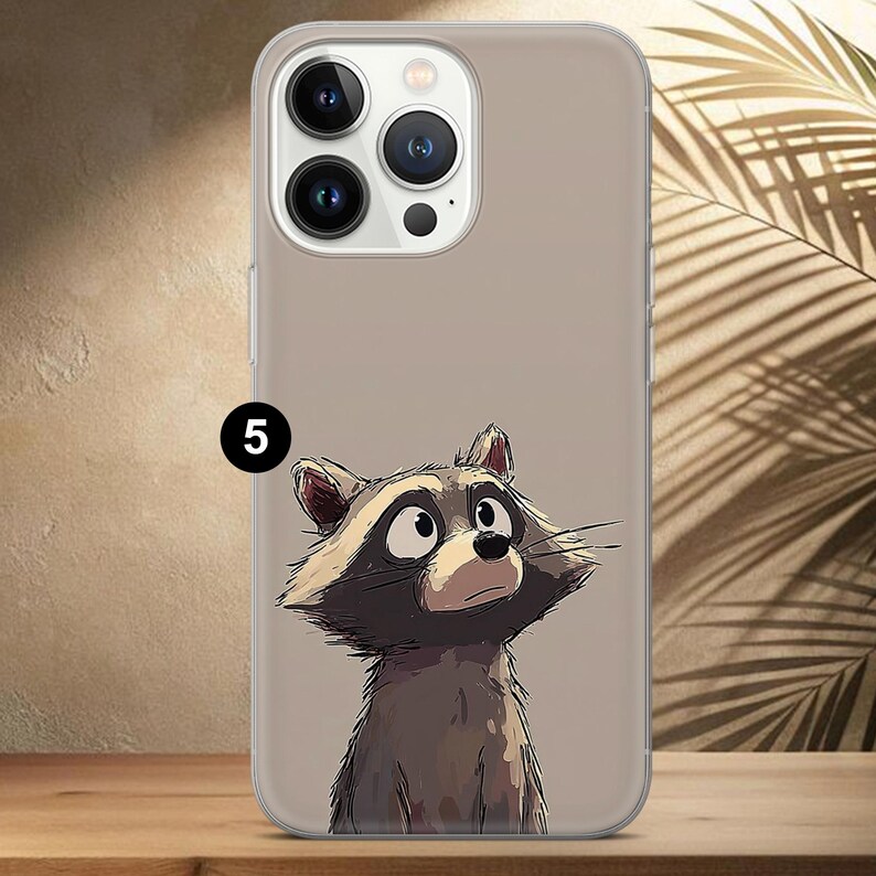 May include: A clear phone case featuring a cartoon raccoon illustration. The raccoon is depicted with a curious expression, in shades of brown, gray, and white. The number "5" is printed in black on the case.
