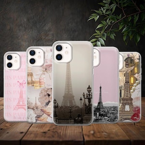Op de afbeelding: Vijf telefoonhoesjes met Parijse ontwerpen. De hoesjes tonen de Eiffeltoren, bloemmotieven en vintage graphics in roze, beige en zwart. Ze worden gepresenteerd op een houten oppervlak, wat een gevoel van Franse elegantie oproept.