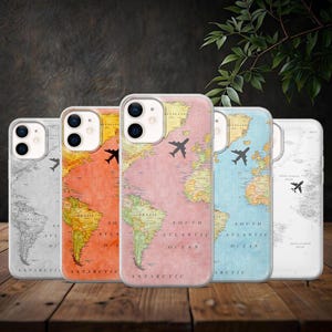 May include: Five phone cases with world map designs in various colors: gray, orange, pink, blue, and white. Each case features a black airplane graphic. The cases are displayed on a wooden surface.
