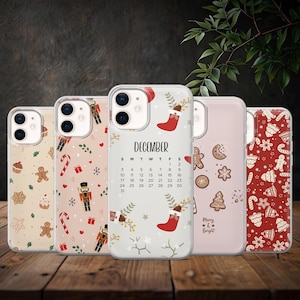 May include: Five phone cases with festive Christmas designs. Patterns include gingerbread men, candy canes, nutcrackers, and a December calendar. One case has the text "Merry & Bright". The cases are on a wooden surface.