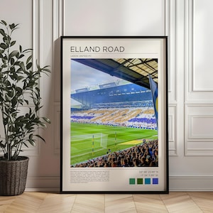 Puede incluir: Impresión enmarcada de Elland Road, sede del Leeds United FC. El estadio está lleno de aficionados, con un campo verde y postes de portería en primer plano. Las gradas están llenas de aficionados vestidos de blanco y amarillo. El cielo está nublado.