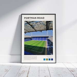 May include: Framed print of Portman Road, home of Ipswich Town FC, featuring a vibrant green pitch and blue seating. The stadium is under a partially covered roof. Text at the top reads "Portman Road". Coordinates and color swatches are at the bottom.