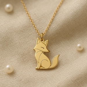 Könnte beinhalten: Goldfarbene Halskette mit einem Fuchsanhänger. Der Anhänger zeigt eine stilisierte Fuchssilhouette mit detailliertem Design. Die Kette ist ebenfalls goldfarben. Der Hintergrund ist ein neutraler Stoff mit drei Perlen.
