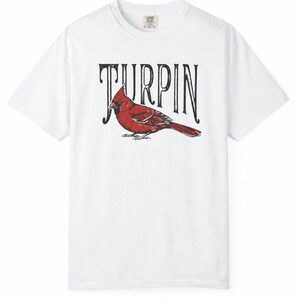 A plain white short-sleeve t-shirt featuring a red cardinal illustration and the black text Turpin on a white background.