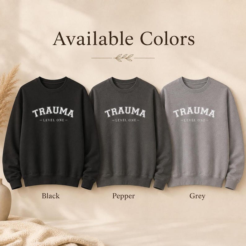Three crewneck sweatshirts in Black, Pepper, and Grey, all featuring the TRAUMA LEVEL ONE design.