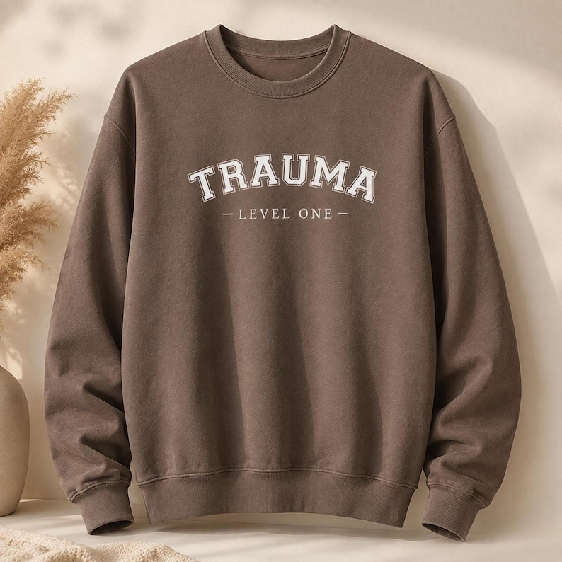 Brown crewneck sweatshirt featuring white text that reads TRAUMA LEVEL ONE.