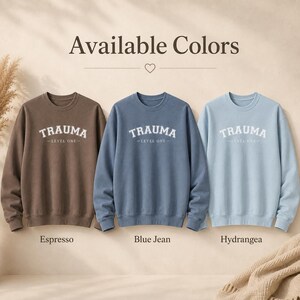 Three crewneck sweatshirts in Espresso, Blue Jean, and Hydrangea with the TRAUMA LEVEL ONE text.